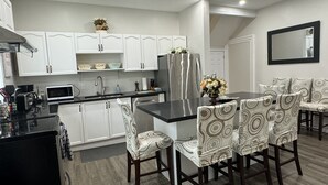 Una cocina moderna con armarios blancos, encimera negra y un refrigerador de acero inoxidable. Hay una zona de comedor con sillas estampadas y una mesa.