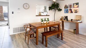 A modern kitchen with a wooden dining table, chairs, and a bench. There is a ceiling fan, a clock, and a plant on the wall.