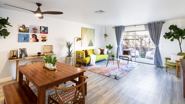 A spacious living room with a wooden dining table, a sofa, and a large window with curtains.