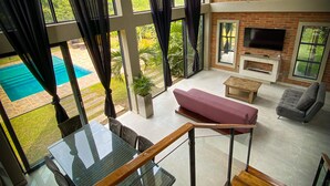 A spacious living area with a glass table, a sofa, and a TV mounted on a brick wall. - ECOPARADISE (Pereira)