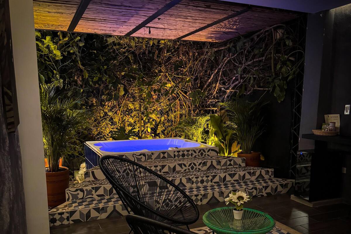 A modern outdoor seating area with a patterned floor, a blue pool, and lush greenery.
