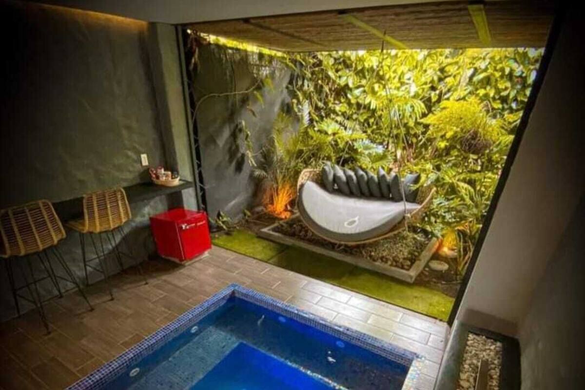 A modern indoor pool area with a hot tub, seating, and a view of a lush garden.