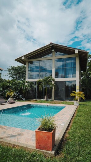 Una casa moderna de dos pisos con piscina, ventanas amplias y césped cuidado.