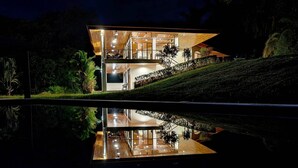 Une maison moderne dotée d’un grand balcon, d’une piscine et dont le reflet se mire dans l’eau.
