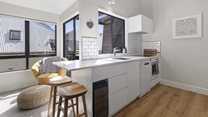 Een moderne keuken met witte kasten, een groot raam en uitzicht op een naburig gebouw.