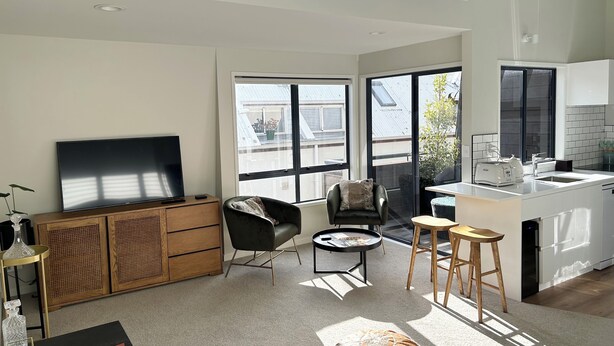 Een moderne woonkamer met een flatscreen televisie, een bank, een salontafel en een eethoek met krukken.