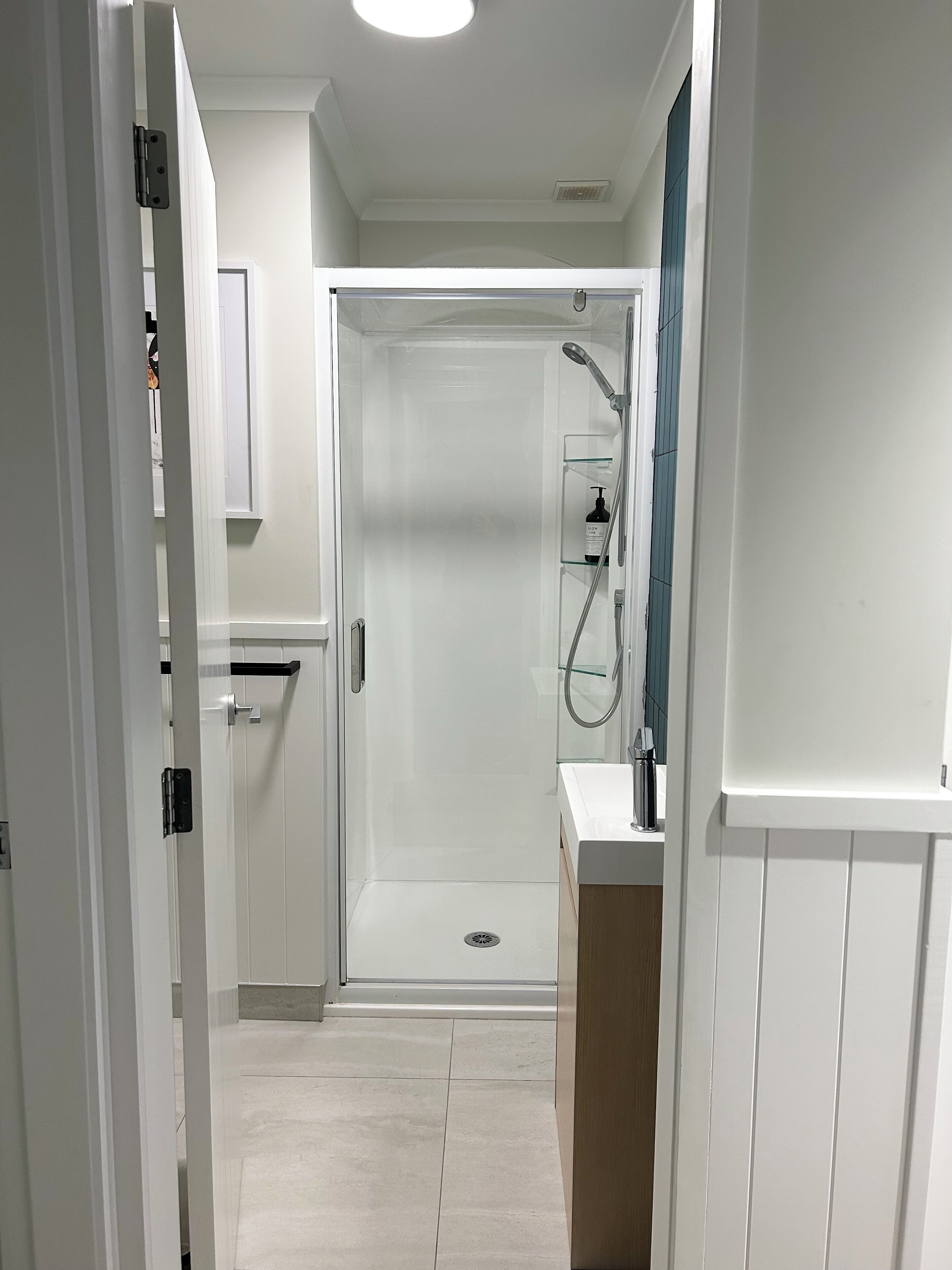 A modern bathroom with a glass-enclosed shower, a white sink, and a small shelf with toiletries.