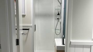A modern bathroom with a glass-enclosed shower, a white sink, and a small shelf with toiletries.