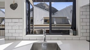Een moderne keuken met een roestvrijstalen spoelbak, een hartvormige decoratie aan de muur en uitzicht op een huis met een metalen dak door een groot raam.