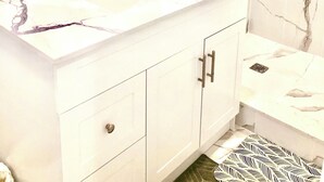 A bathroom with a white vanity, a mirror, a shower, and a patterned floor mat. - Cozy Home (Markham)