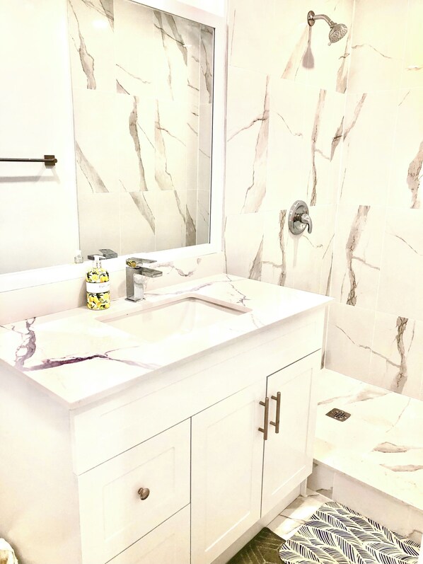 A bathroom with a white vanity, a mirror, a shower, and a patterned floor mat. - Cozy Home (Markham)