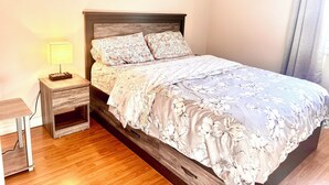 A neatly made bed with floral bedding, a bedside table with a lamp, and a wooden nightstand. - Cozy Home (Markham)