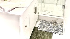 A bathroom with a marble vanity, a shower with glass doors, and a patterned rug. - Cozy Home (Markham)