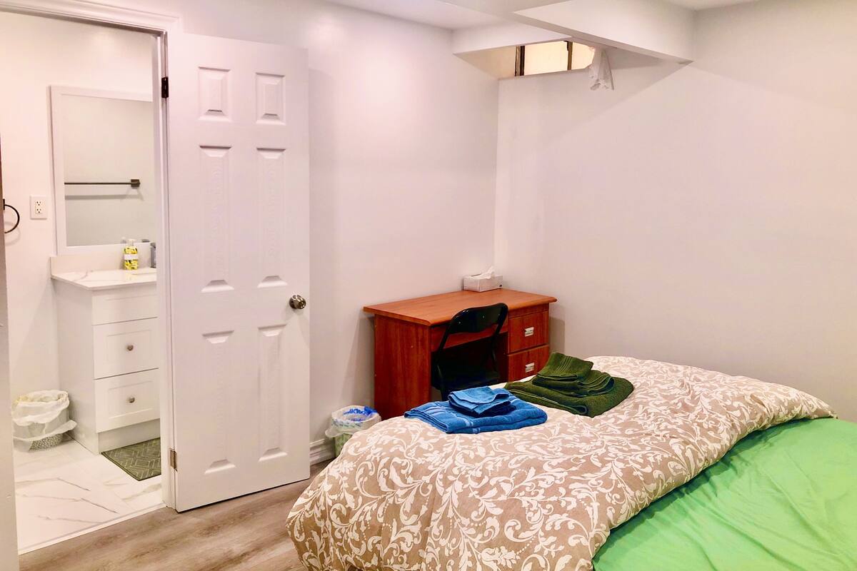 A bedroom with a bed, a wooden desk, a chair, a wardrobe, and a door.