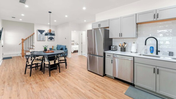 A modern kitchen with stainless steel appliances, grey cabinets, and a wooden dining table.