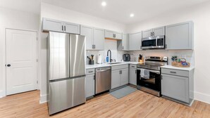 A modern kitchen with stainless steel appliances, grey cabinetry, and wooden flooring.