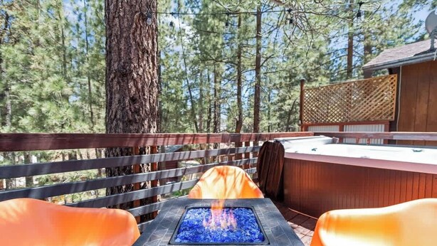 An outdoor deck with a fire feature, seating, and a view of trees.