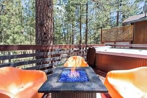 Um deck externo com lareira, assentos e vista para árvores.