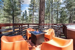A deck with a fire feature, orange chairs, and a view of a forest.