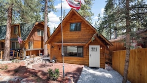 A wooden cabin with a flag, a patio, and a fenced yard.