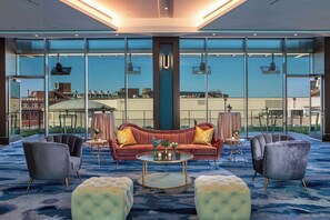 Een moderne hotel lobby met een grote glazen wand, een rode bank, twee fauteuils en een ronde salontafel.