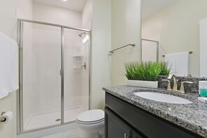 Ein modernes Badezimmer mit einer gläsernen Duschkabine, einer weißen Toilette, einem Waschtisch mit Granitplatte und einem Blumentopf.