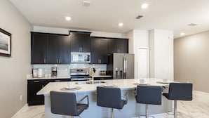 A modern kitchen with dark cabinets, a central island with bar stools, and stainless steel appliances. - 8957sid-the Retreat At Championsgate 4 Bedroom Townhouse by RedAwning (Davenport)
