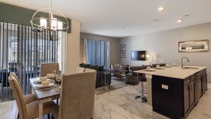 A modern kitchen with a central island, dining area with chairs and table, and a living area with sofas and a TV. - 8957sid-the Retreat At Championsgate 4 Bedroom Townhouse by RedAwning (Davenport)