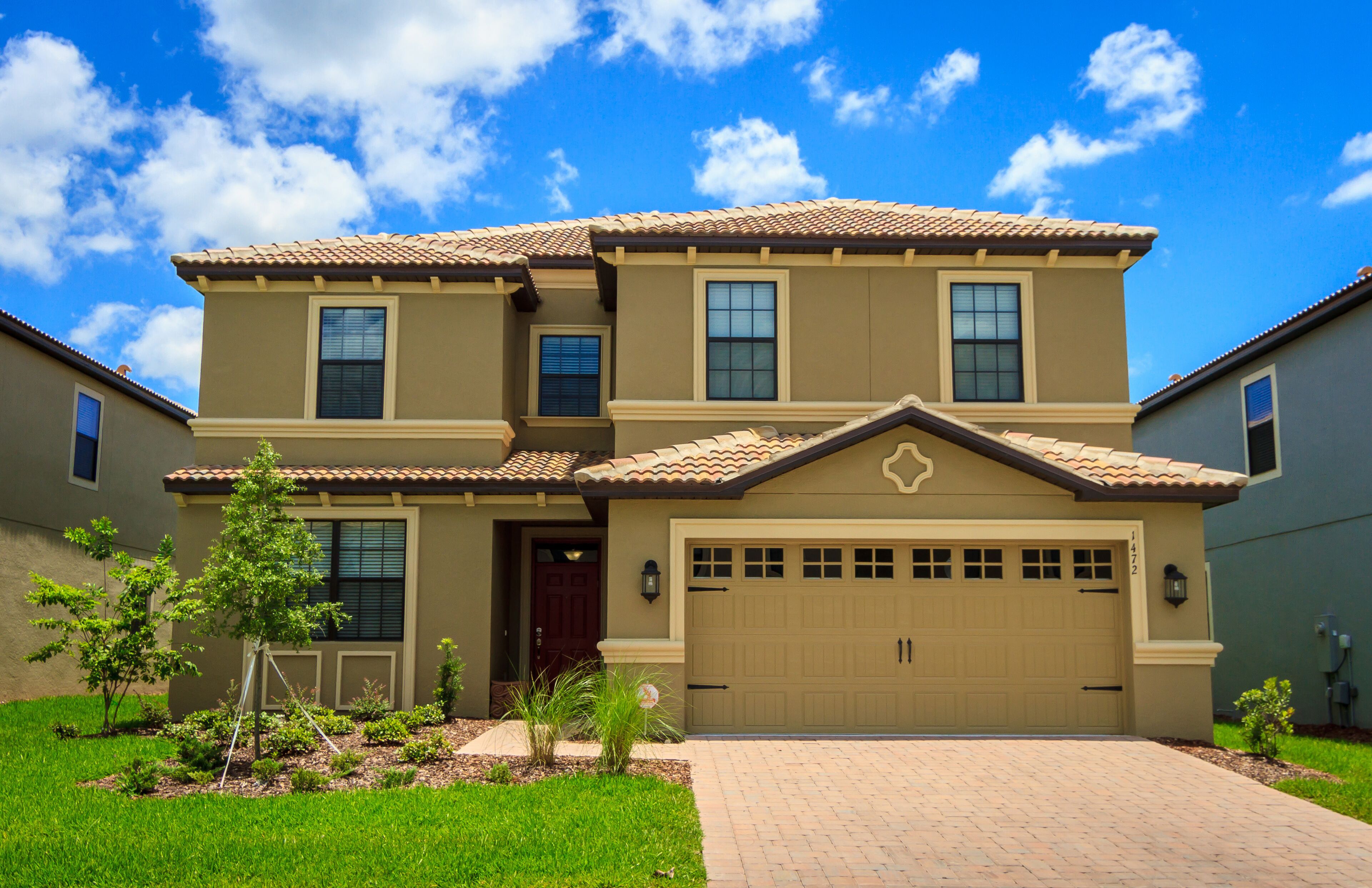 A two-story house with a beige exterior, a tiled roof, and a garage.