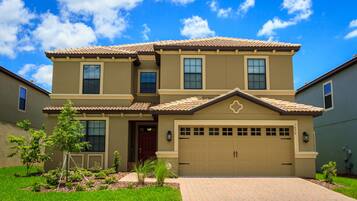 A two-story house with a beige exterior, a tiled roof, and a garage.