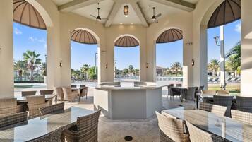 An outdoor patio area with wicker furniture and a central island, surrounded by arches and ceiling fans.