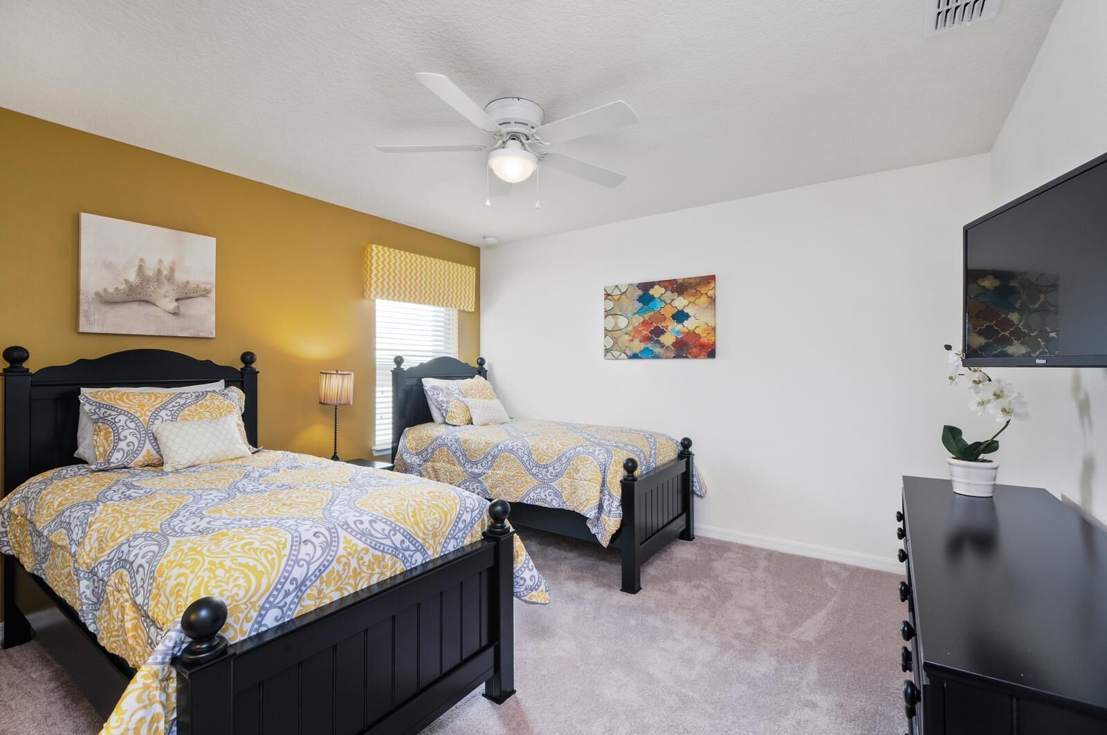 A bedroom with two beds, a ceiling fan, artwork on the walls, and a TV on a dresser.