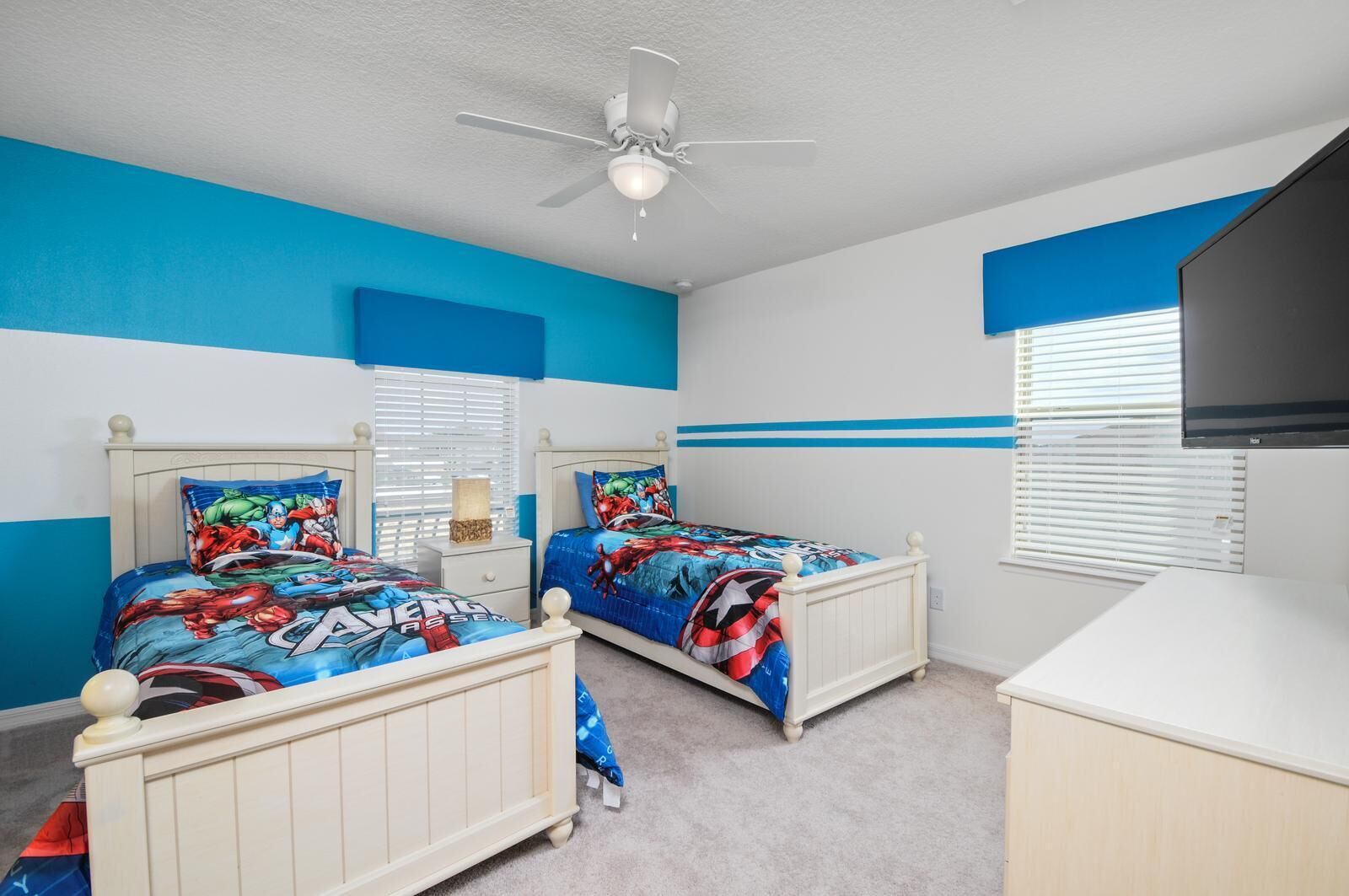 A bedroom with two beds, a ceiling fan, a TV, and a window with blinds.