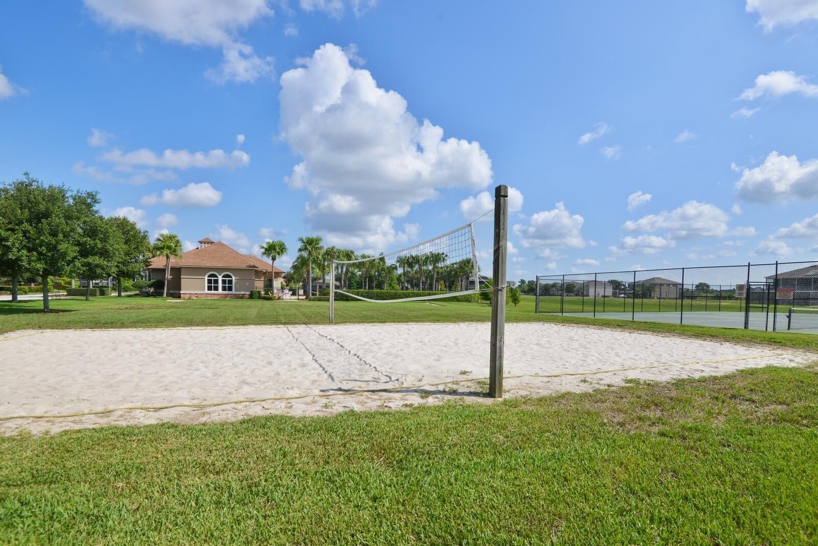 A volleyball court with a net, surrounded by a sandy area and a grassy field.