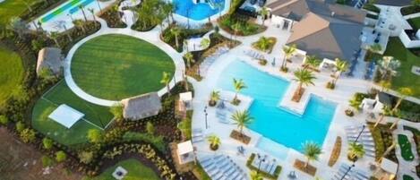An aerial view of a resort with a large swimming pool, a water park, and a tennis court.