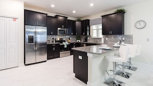 A modern kitchen with dark cabinets, stainless steel appliances, and a large island with bar stools. - 9038sid-the Retreat At Champions Gate 6 Bedroom Villa by RedAwning (Davenport)