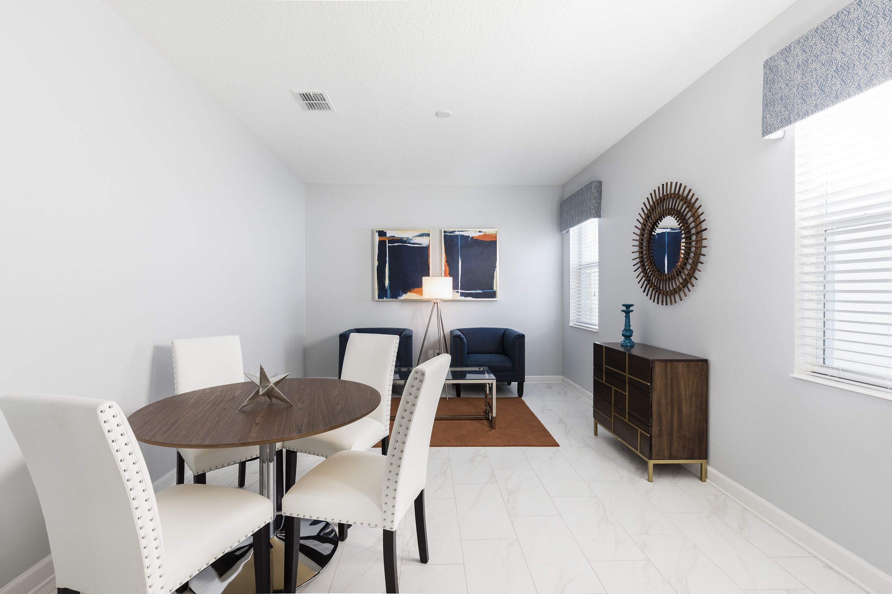 A modern dining area with a round table, white chairs, a blue sofa, and a wooden cabinet.
