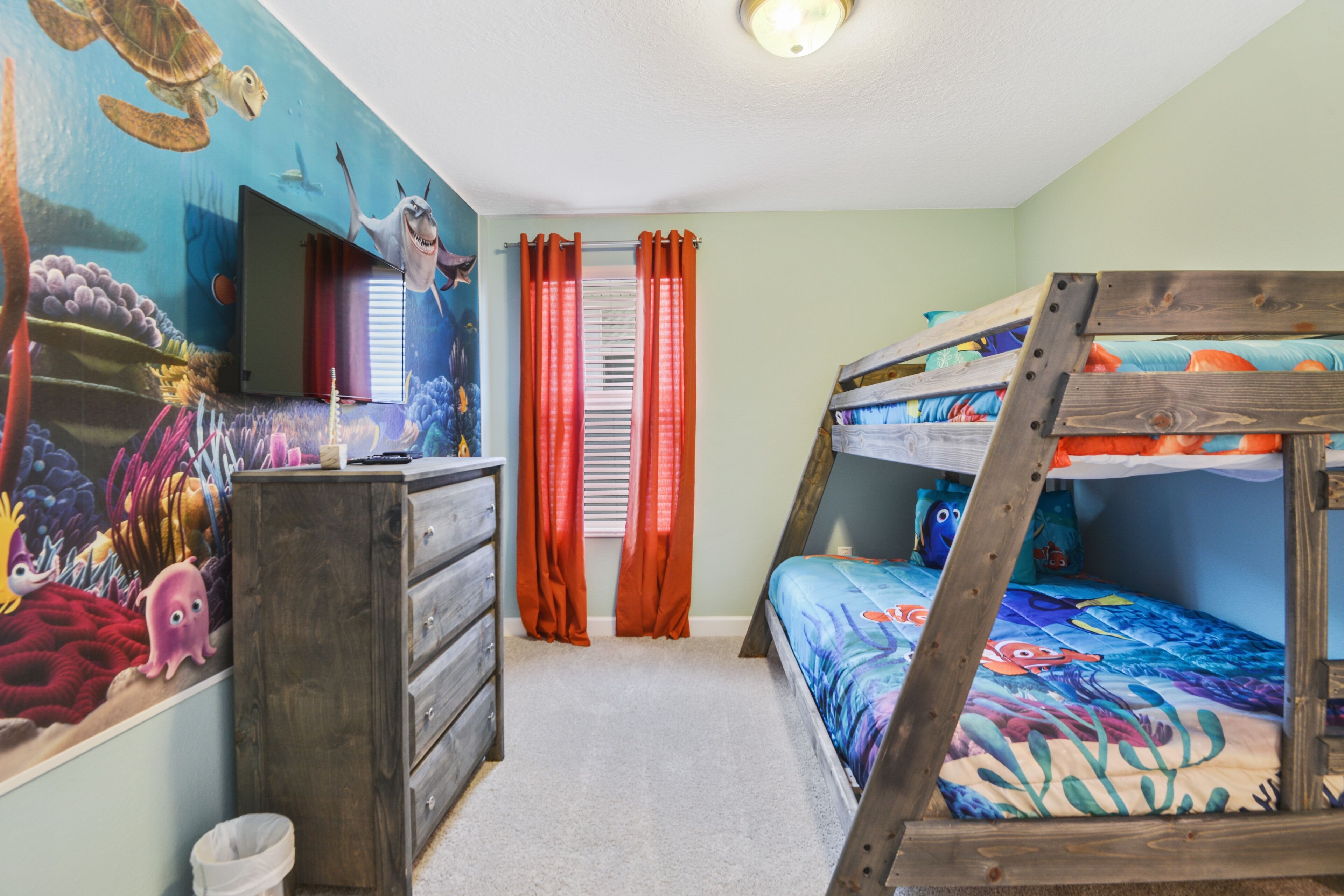 A child's bedroom with a mural, bunk beds, a dresser, and a TV.