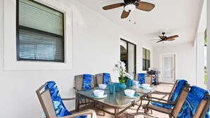Eine überdachte Terrasse mit einem Glastisch, Stühlen und Deckenventilatoren.