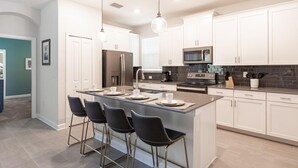 A modern kitchen with white cabinets, a central island with bar stools, stainless steel appliances, and pendant lighting.