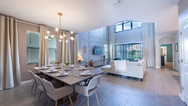 A modern dining area with a large table set for six, surrounded by grey upholstered chairs.