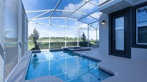 A modern outdoor swimming pool with a glass enclosure, surrounded by a white building with a black door and windows.