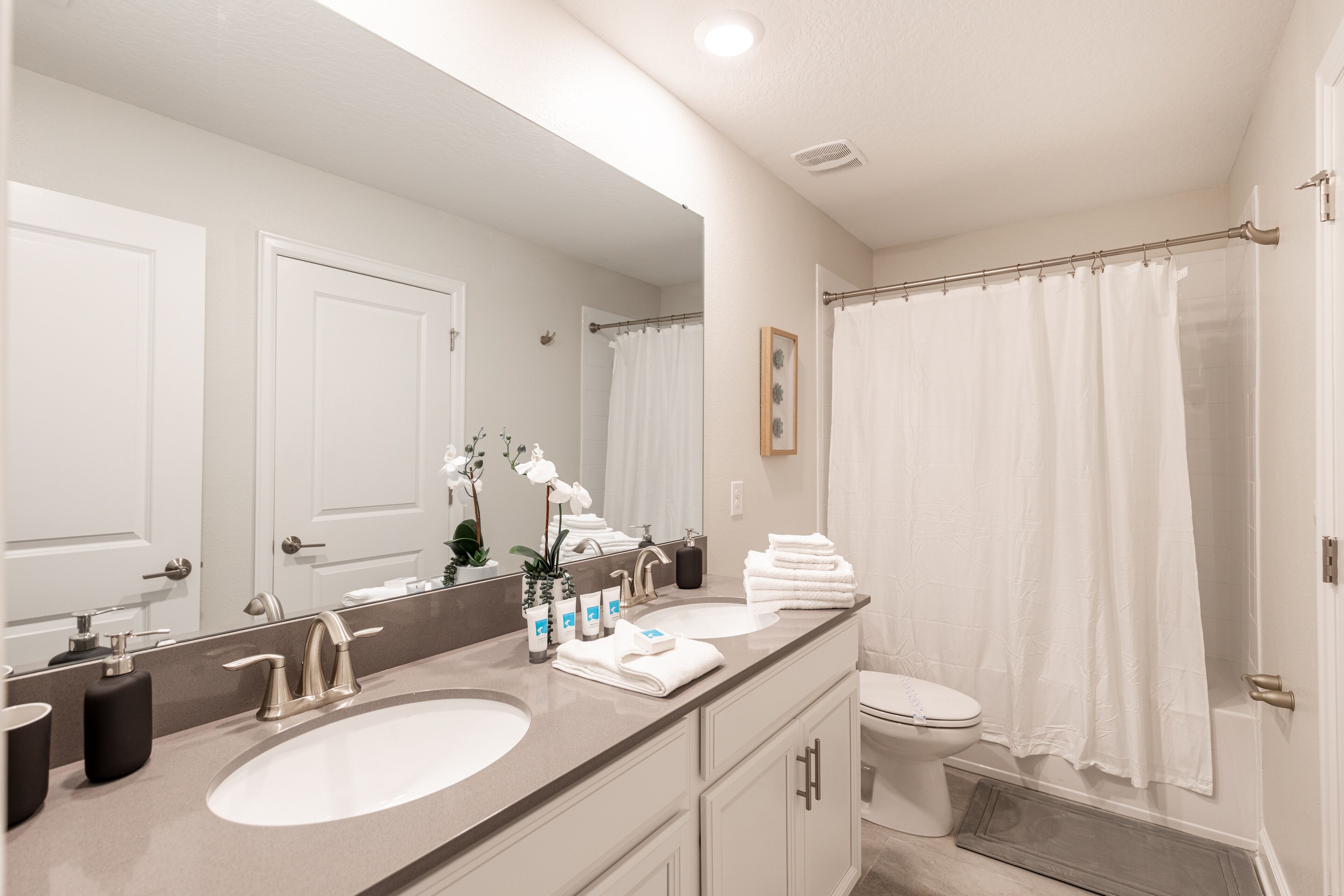 Une salle de bain avec un double lavabo, des toilettes, un rideau de douche et un grand miroir.