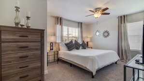 A bedroom with a bed, dresser, ceiling fan, bedside lamps, and decorative wall mirrors. - 1589mvd-the Retreat At Championsgate 4 Bedroom Townhouse by RedAwning (Davenport)
