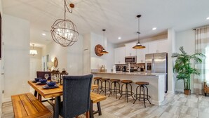 A modern kitchen with white cabinets, stainless steel appliances, and a central island with stools. - 1589mvd-the Retreat At Championsgate 4 Bedroom Townhouse by RedAwning (Davenport)