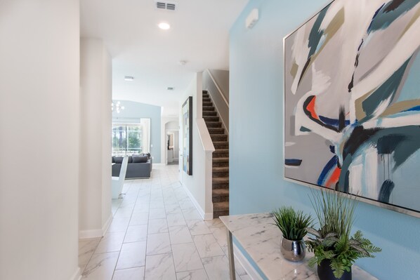 A modern interior with a marble floor, a staircase, and a large abstract painting on the wall. - 601dsd-the Retreat At Championsgate 5 Bedroom Home by RedAwning (Kissimmee)