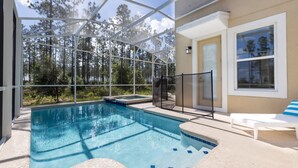 A swimming pool with a glass enclosure, surrounded by a beige wall and a white lounge chair with a striped cushion.