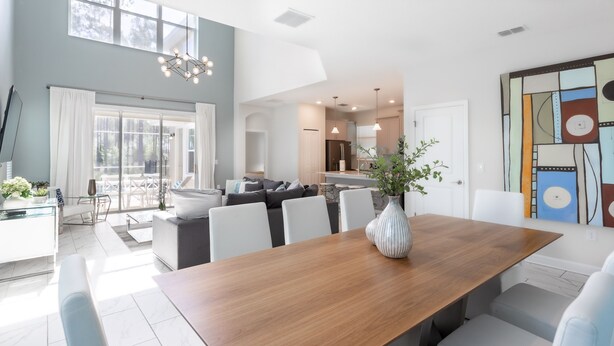 A modern living room with a wooden dining table, white sofas, and a large window.
