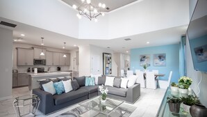 A modern living room with a sectional sofa, glass coffee table, and a dining area with a white table and chairs.