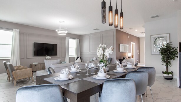 A modern dining room with a dark wooden table set for six, surrounded by grey upholstered chairs. - 9028sh-the Retreat At Championsgate 6 Bedroom Home by RedAwning (Davenport)